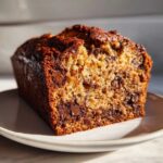 A close-up, sunlit slice of moist chocolate banana bread showing a rich crumb and melted chocolate chips.