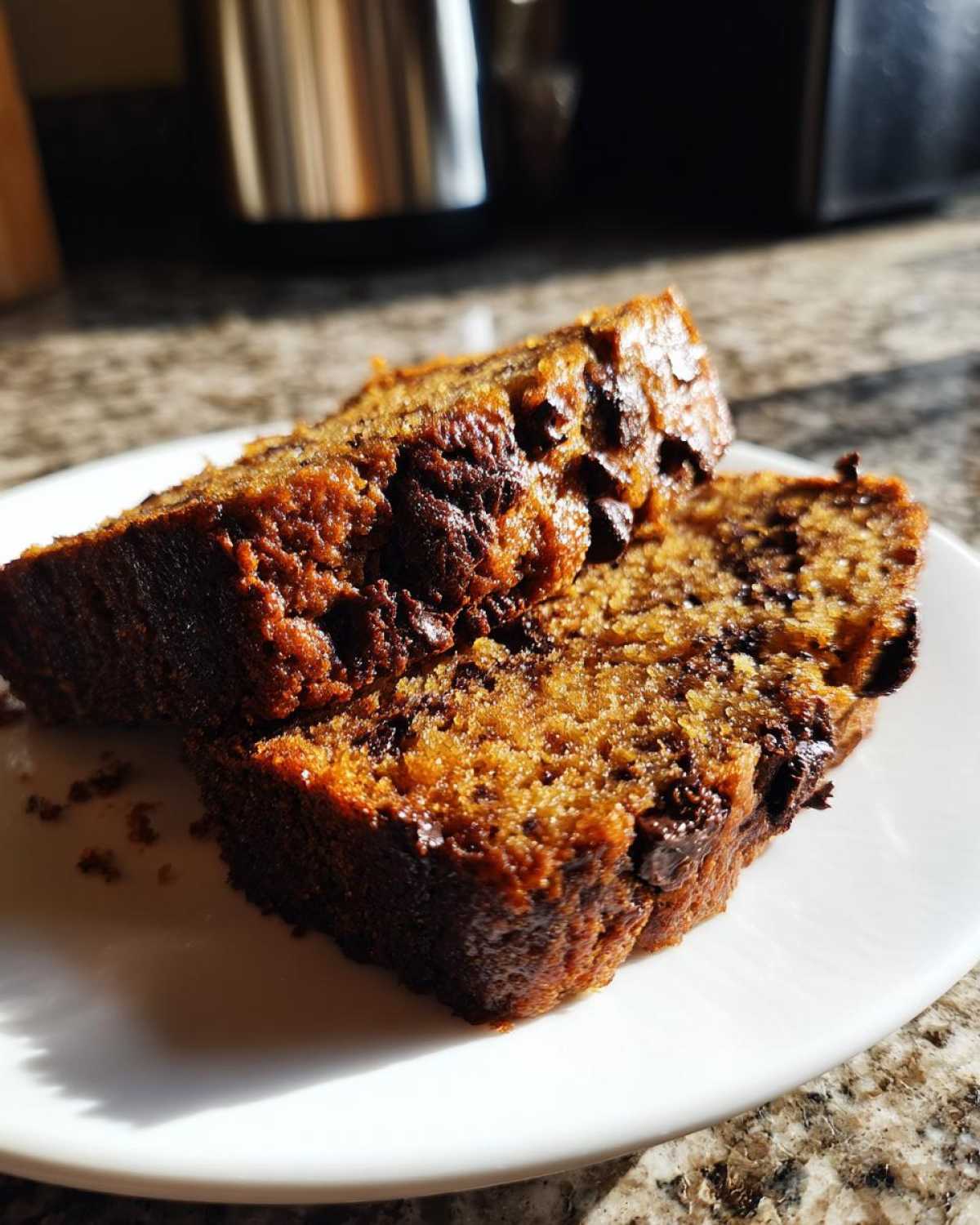 Two moist slices of chocolate banana bread with visible chocolate chips, served on a white plate.