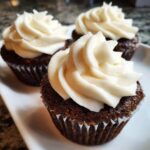 Close-up of three moist gingerbread cupcakes topped with swirls of creamy white frosting.