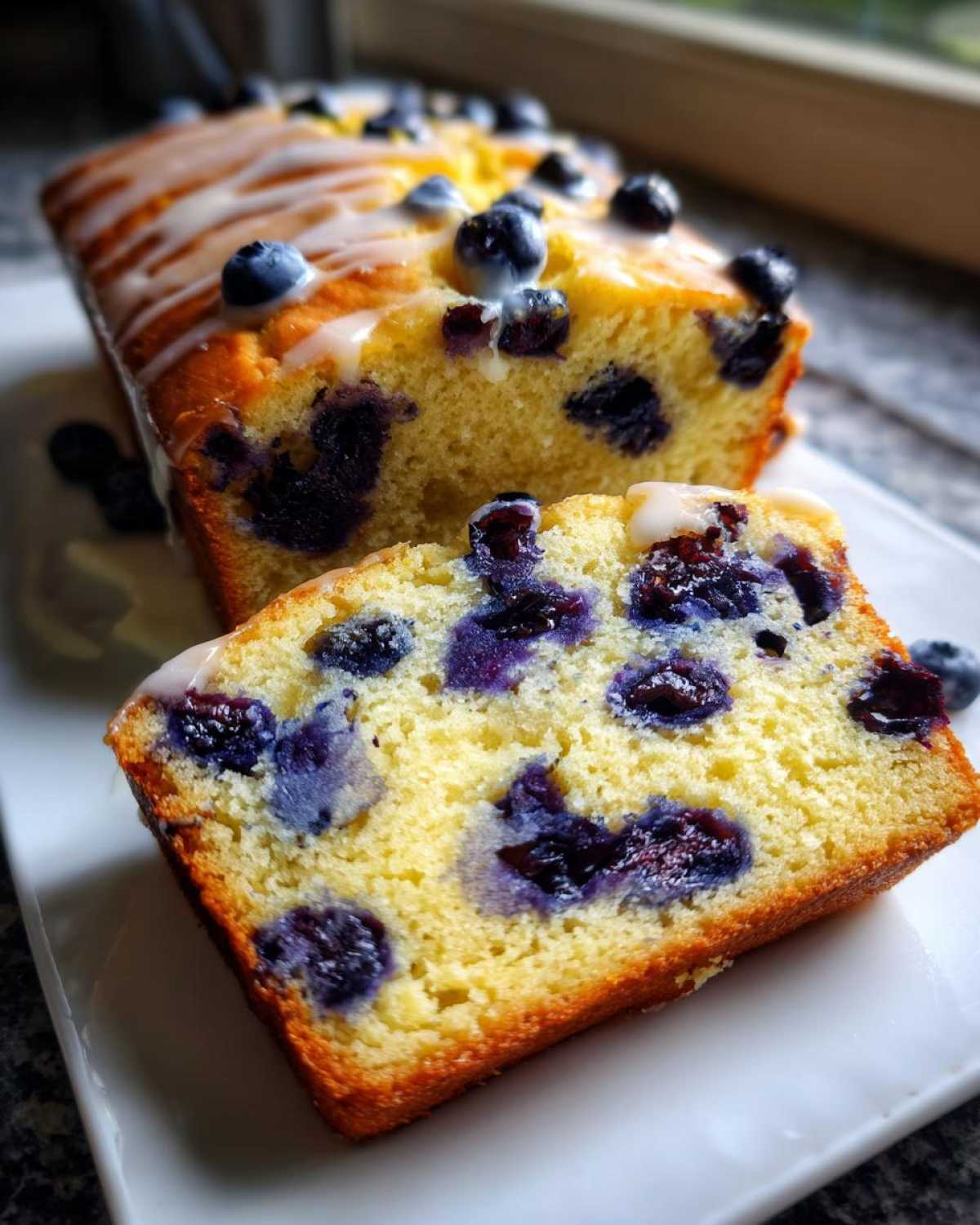 Close-up of a slice of moist lemon blueberry bread, showing vibrant blueberries and a light lemon glaze.