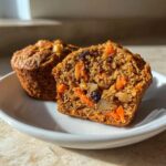 Close-up of a moist morning glory muffin cut in half showing carrots, raisins, and nuts inside.