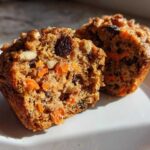 Close-up of a morning glory muffin cut in half showing moist texture, shredded carrots, raisins, and walnuts.