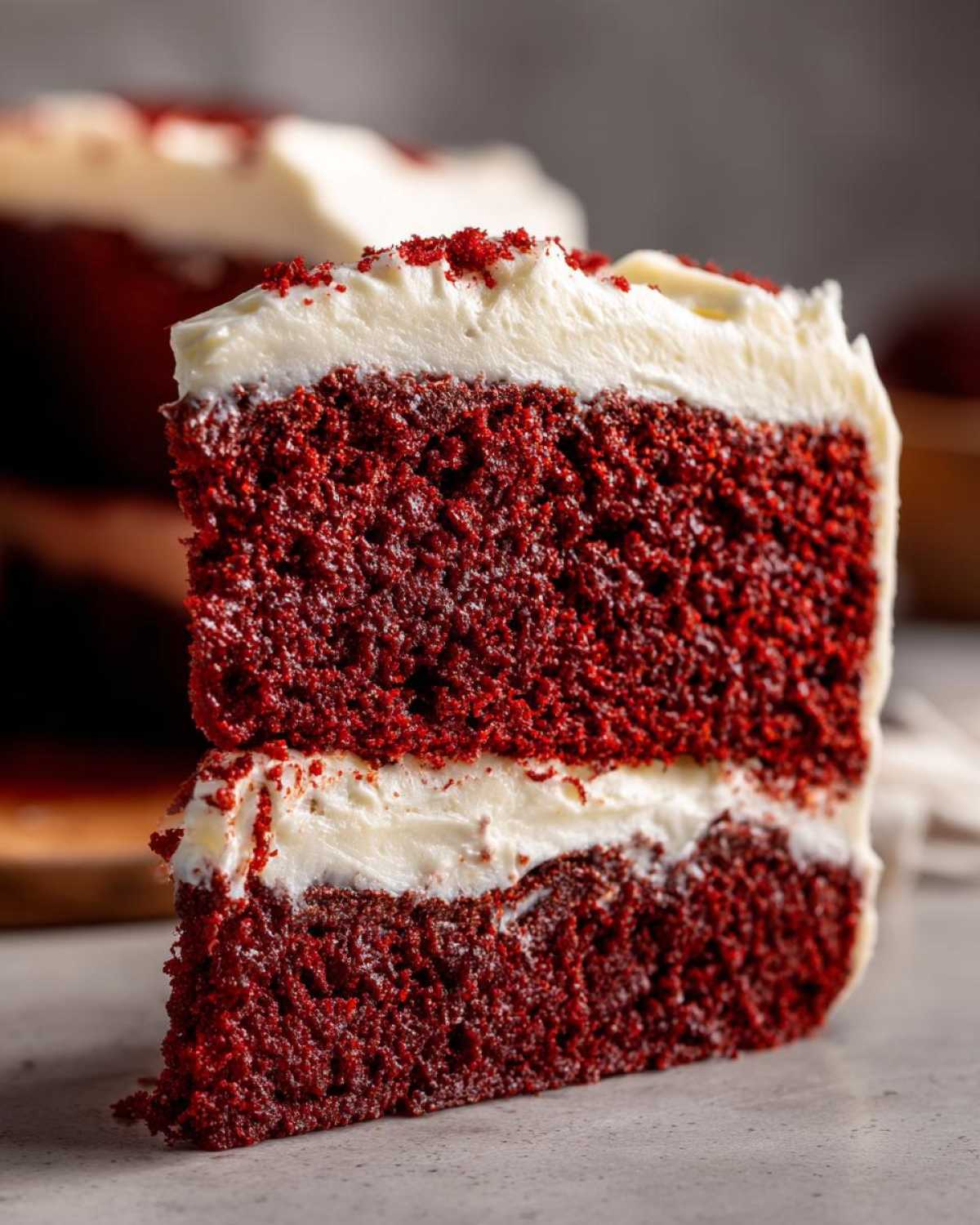 Close-up of a moist slice of red velvet cake showing two vibrant red layers separated by thick cream cheese frosting.