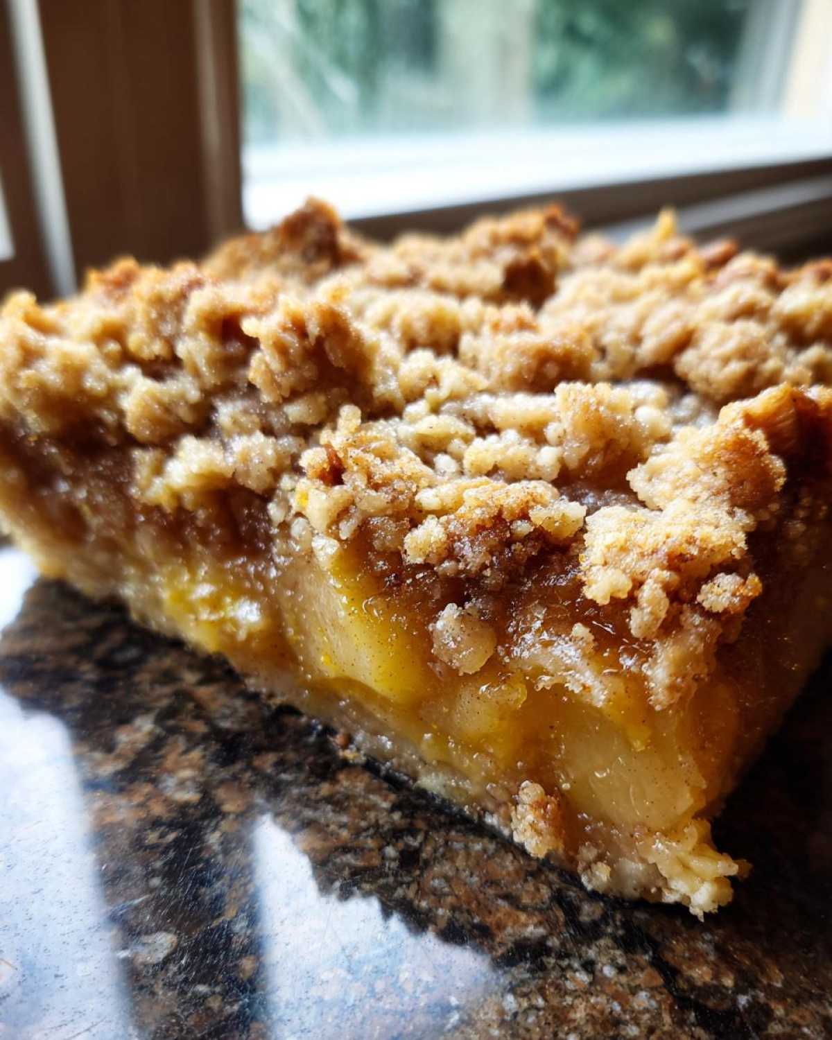 Close-up of a moist slice of pear crisp showing tender fruit filling and a thick, crunchy brown sugar crumble topping.