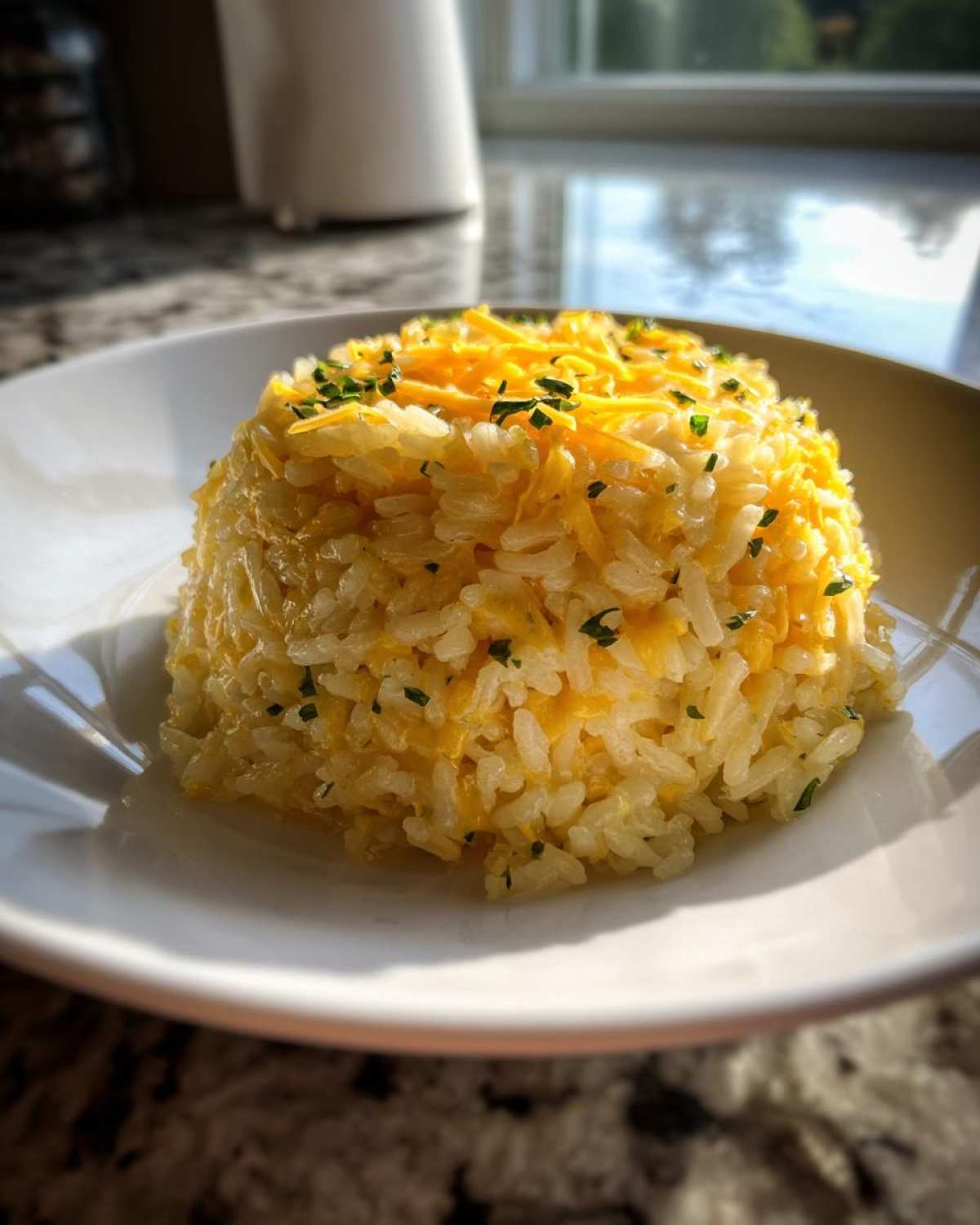 A molded serving of fluffy white rice topped generously with shredded cheddar cheese and chopped chives, showcasing delicious cheesy rice.