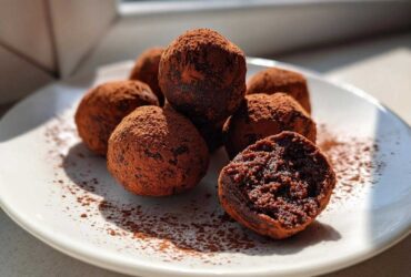 A pile of rich, dark chocolate protein balls dusted heavily with cocoa powder on a white plate.