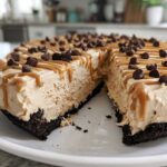 A slice removed from a creamy no-bake peanut butter pie topped with caramel drizzle and chocolate chips.