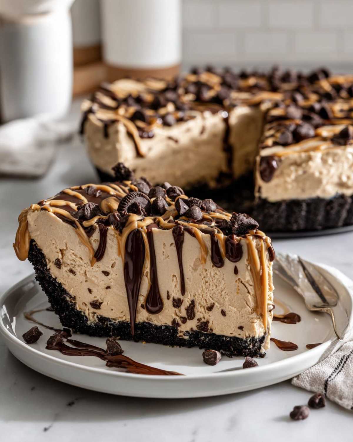 A decadent slice of no-bake peanut butter pie with a dark crust, topped with chocolate chips and drizzles.