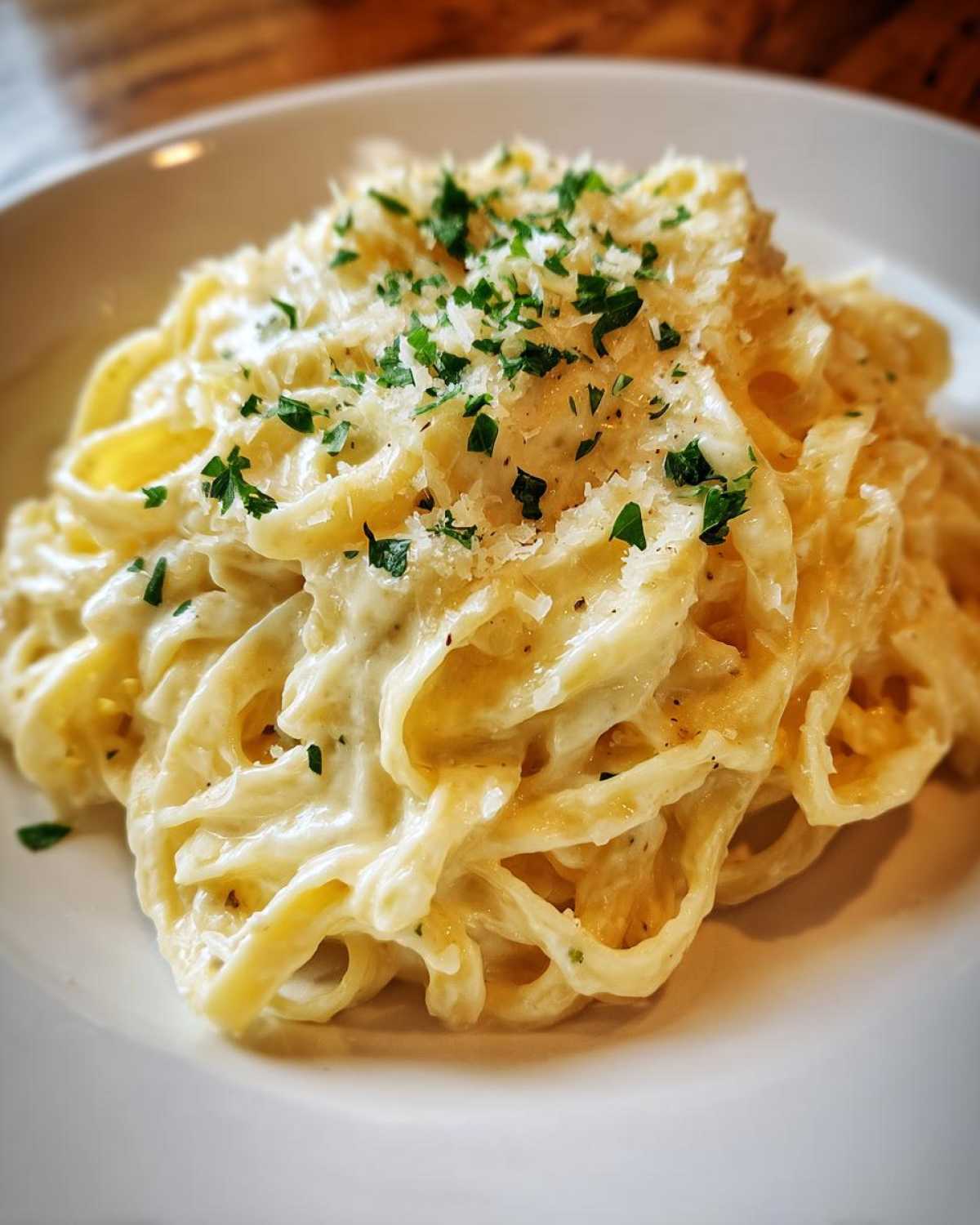 Close-up of fettuccine pasta generously coated in creamy Olive Garden Alfredo Sauce, topped with grated Parmesan and parsley.