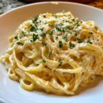 Close-up of fettuccine pasta coated in rich, creamy Olive Garden Alfredo Sauce, topped with Parmesan and parsley.