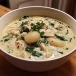 A close-up of a white bowl filled with creamy olive garden chicken gnocchi soup, featuring chicken, spinach, and potato gnocchi.