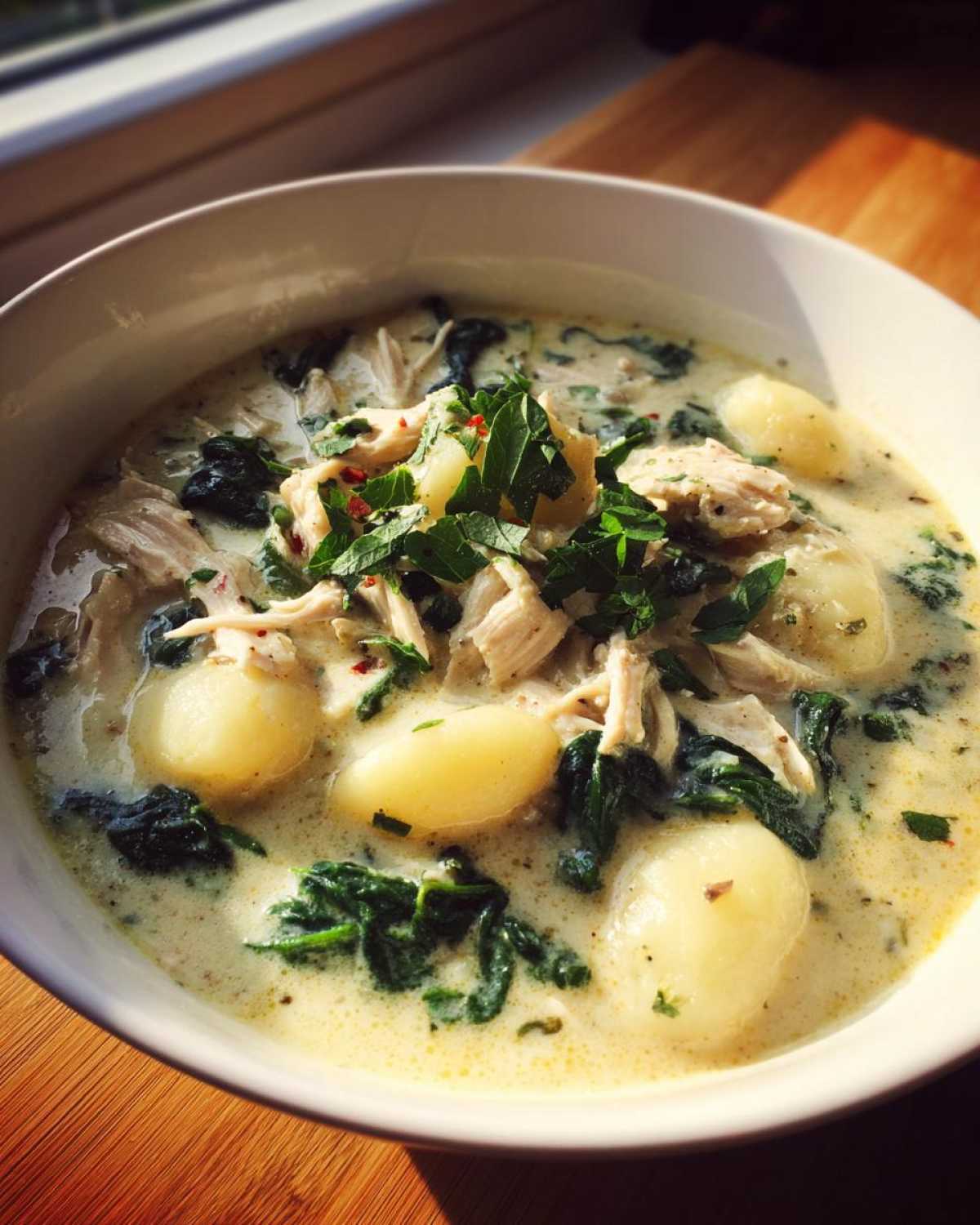 A close-up of creamy olive garden chicken gnocchi soup, topped with fresh parsley and chili flakes.
