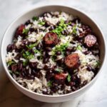Close-up of a bowl filled with flavorful black beans and rice mixed with slices of smoked sausage and garnished with fresh cilantro.