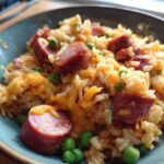 Close-up of a bowl of cheesy sausage and rice delight with bright green peas.