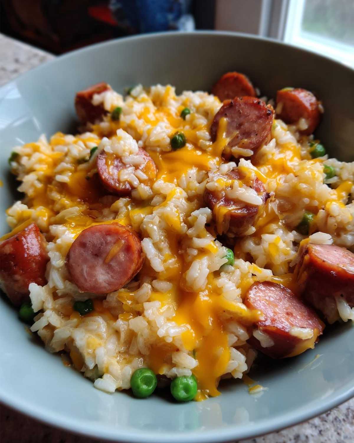 Close-up of a bowl of cheesy sausage and rice mixed with green peas.