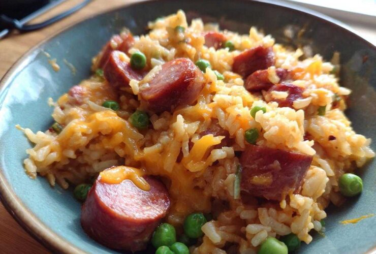 Close-up of a bowl of cheesy sausage and rice delight with bright green peas.