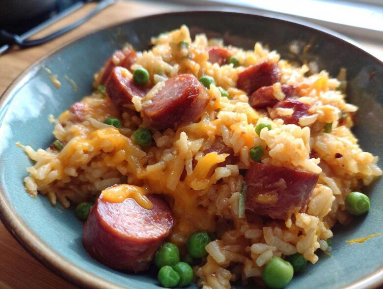 Close-up of a bowl of cheesy sausage and rice delight with bright green peas.