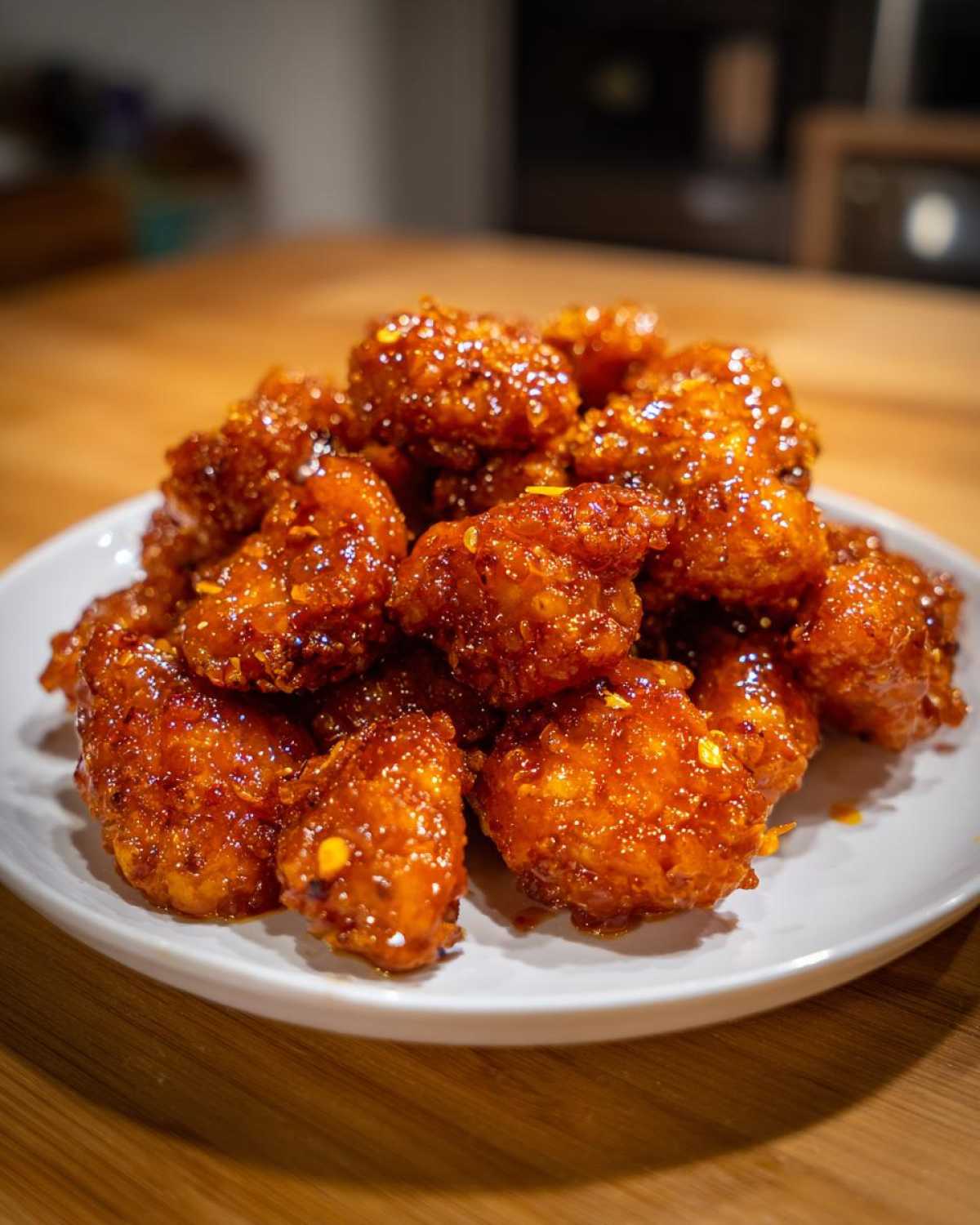 A pile of crispy, glazed pieces of orange chicken recipe served on a white plate.