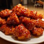Close-up of crispy pieces of orange chicken recipe coated in a thick, shiny orange glaze and sprinkled with sesame seeds.