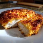 Close-up of parmesan crusted chicken cut in half showing juicy white meat inside the crispy golden-brown coating.