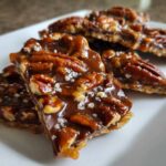 Close-up of several pieces of rich Pecan Pie Bark topped with whole pecans, caramel, and flaky sea salt.