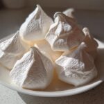 A pile of crisp, white meringue cookies with sharp peaks displayed on a small white plate.