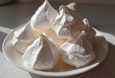 A pile of crisp, white meringue cookies with sharp peaks displayed on a small white plate.