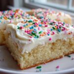 Close-up of thick, moist sugar cookie bars topped with white frosting and colorful sprinkles.