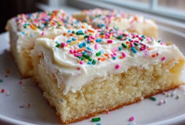 Close-up of thick, moist sugar cookie bars topped with white frosting and colorful sprinkles.