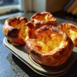Four golden brown, perfectly risen yorkshire pudding puffs fresh out of the oven in a metal muffin tin.