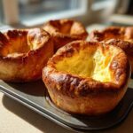 Four golden brown, perfectly risen yorkshire pudding puffs sitting in a muffin tin near a window.