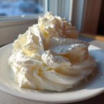 A large swirl of bright white, fluffy cream cheese frosting piped high in a small white bowl.