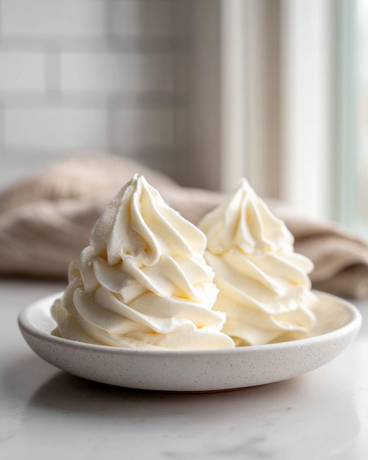 Two perfect swirls of creamy vanilla buttercream frosting piped onto a small white speckled bowl.
