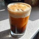 A tall glass filled with rich, dark pumpkin cream cold brew coffee topped with frothy foam.
