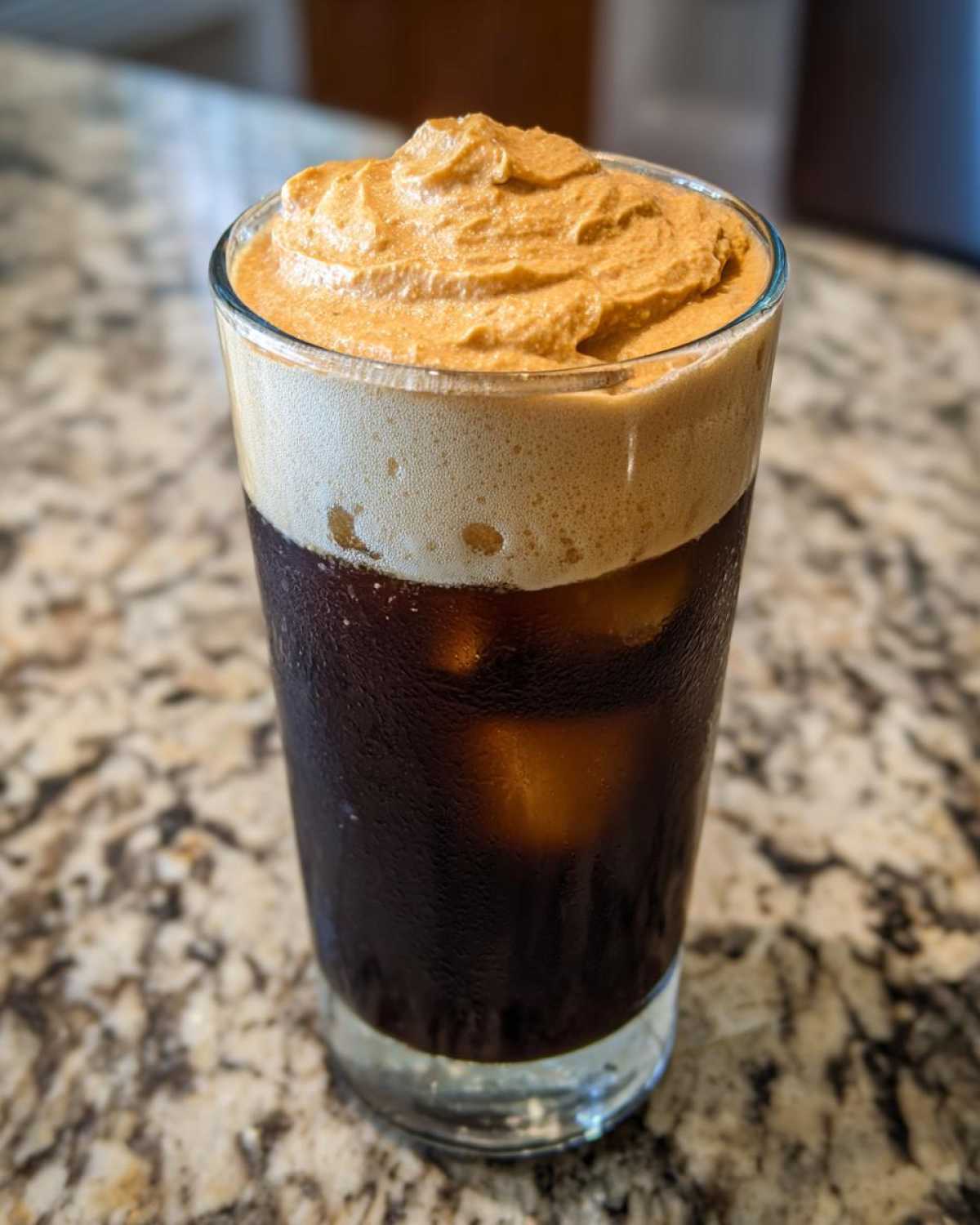 Close-up of a tall glass filled with iced coffee and topped with thick, whipped pumpkin cream cold brew foam.