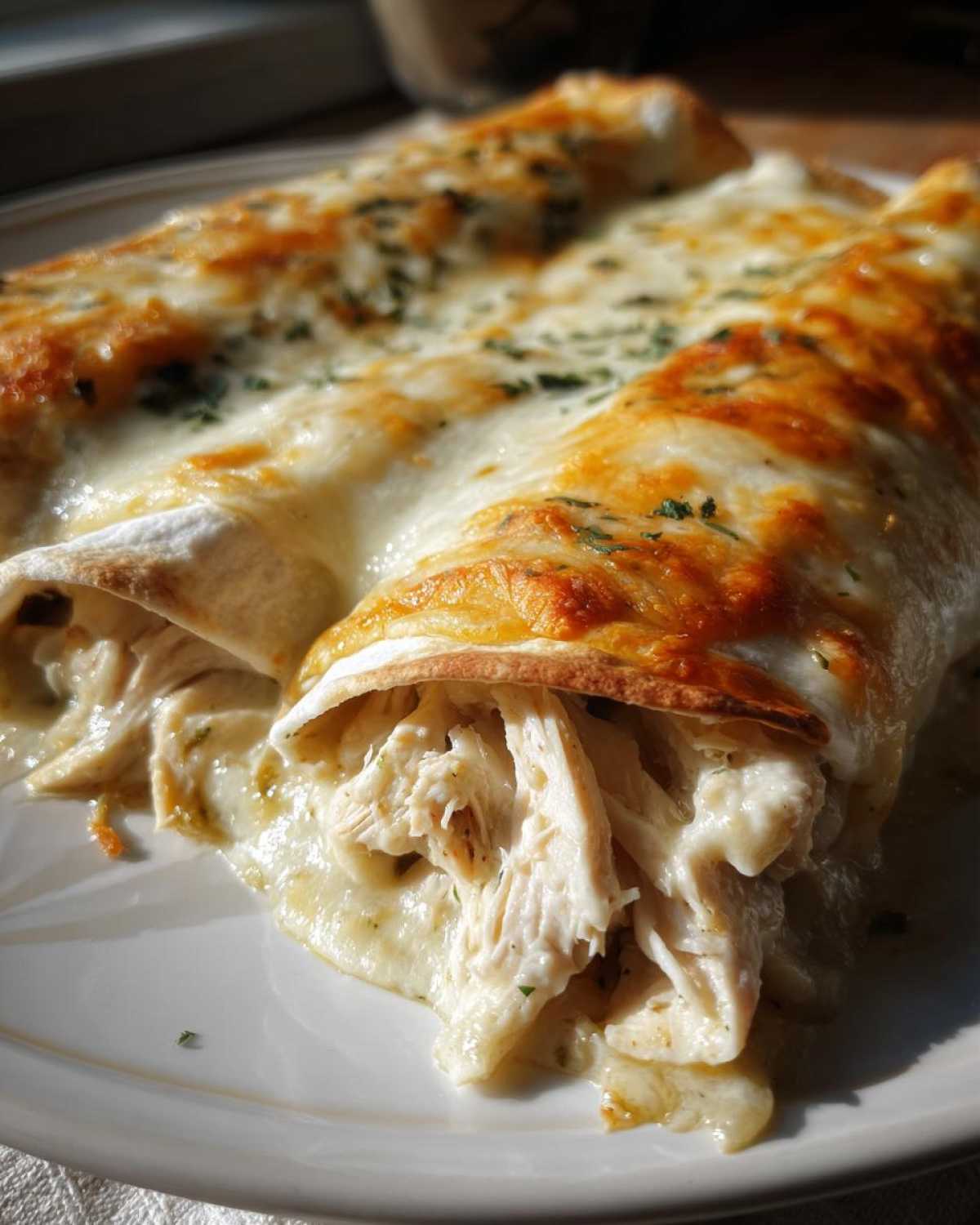 Close-up of two delicious chicken enchiladas smothered in melted white cheese and herbs.