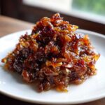 A close-up mound of deeply browned, glossy caramelized onions served on a small white plate.