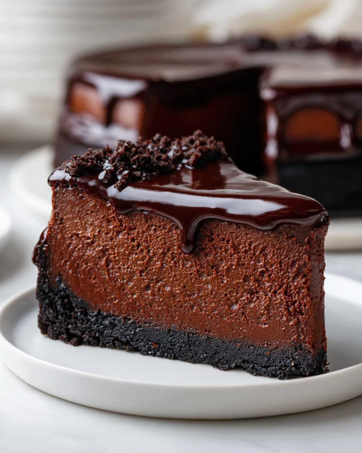 A decadent slice of chocolate cheesecake with a dark crust, topped with glossy chocolate ganache and crumbles.
