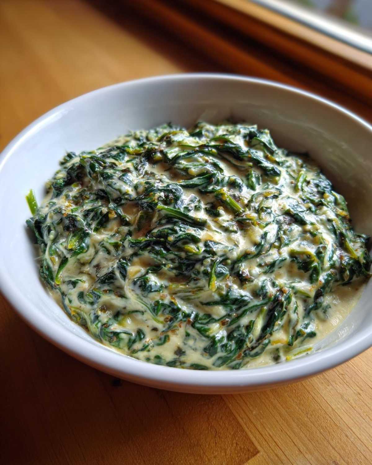 A close-up of a white bowl filled with rich, homemade creamed spinach recipe.