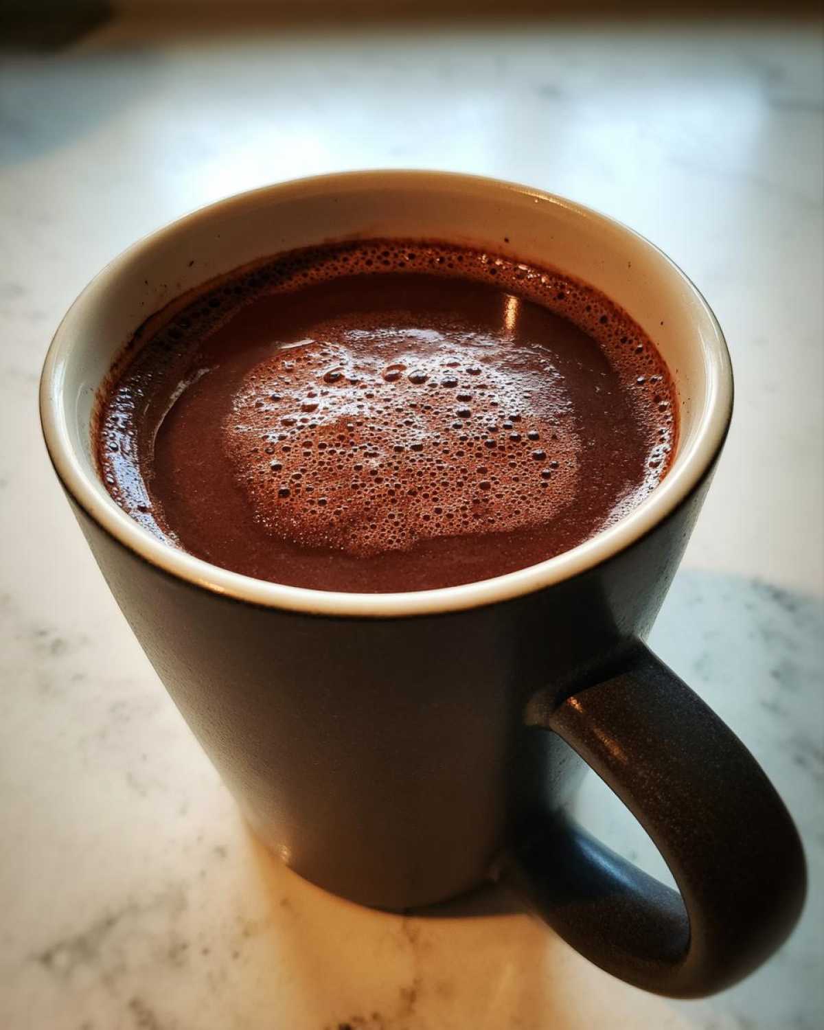 Close-up of a dark mug filled with rich, frothy homemade hot cocoa.