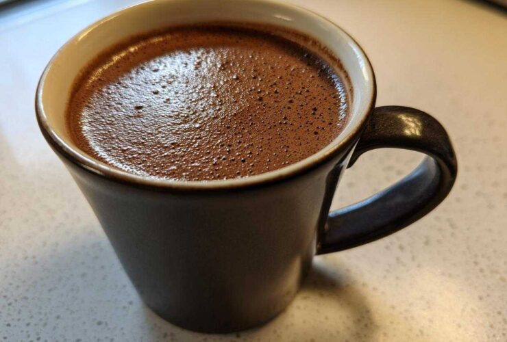 Close-up of a dark mug filled with frothy homemade hot cocoa resting on a light countertop.
