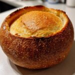 Close-up of a perfectly baked, round bread bowl with a dark, crackled crust and a golden top.