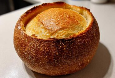 Close-up of a perfectly baked, round bread bowl with a dark, crackled crust and a golden top.