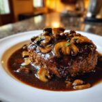 A close-up of a perfectly cooked Salisbury steak smothered in rich brown gravy and sliced mushrooms.