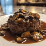 A perfectly cooked Salisbury steak smothered in rich mushroom gravy, served on a white plate.