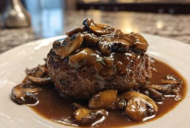 A perfectly cooked Salisbury steak smothered in rich mushroom gravy, served on a white plate.