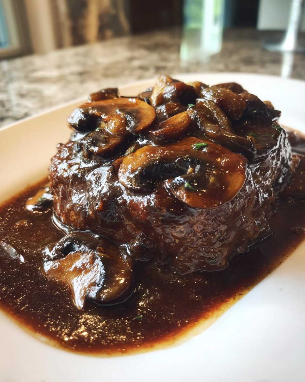 Close-up of a juicy Salisbury steak smothered in dark mushroom gravy on a white plate.