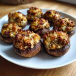 A close-up of seven baked Sausage stuffed mushrooms with golden-brown, cheesy topping served on a white plate.