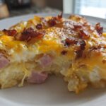 Close-up of a serving of scalloped potatoes and ham, topped with melted cheddar cheese and crispy bacon pieces.