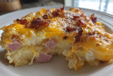 Close-up of a serving of scalloped potatoes and ham, topped with melted cheddar cheese and crispy bacon pieces.